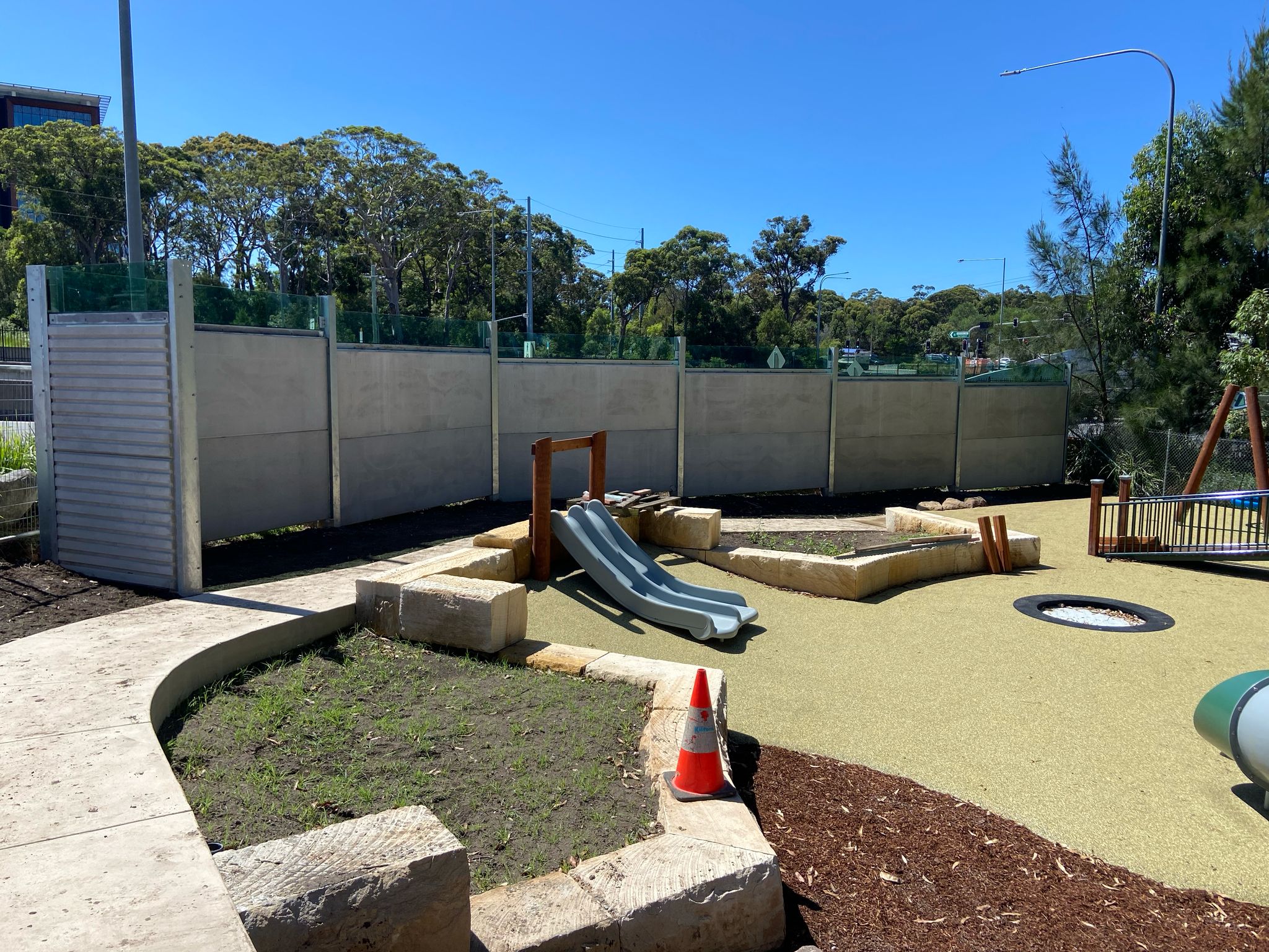 A concrete noise barrier wall with a playground setting in the foreground. It was made by Wallmark Heuron Group.