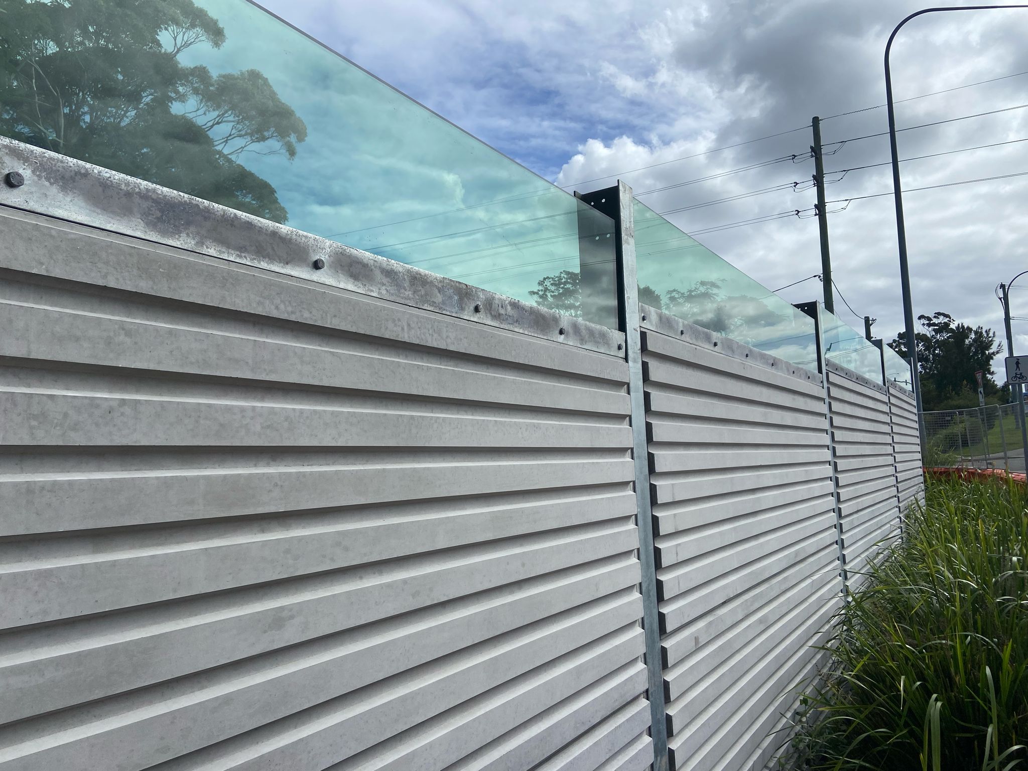 A concrete noise barrier wall with a section of perspex along the top. It was made by Wallmark Heuron Group.